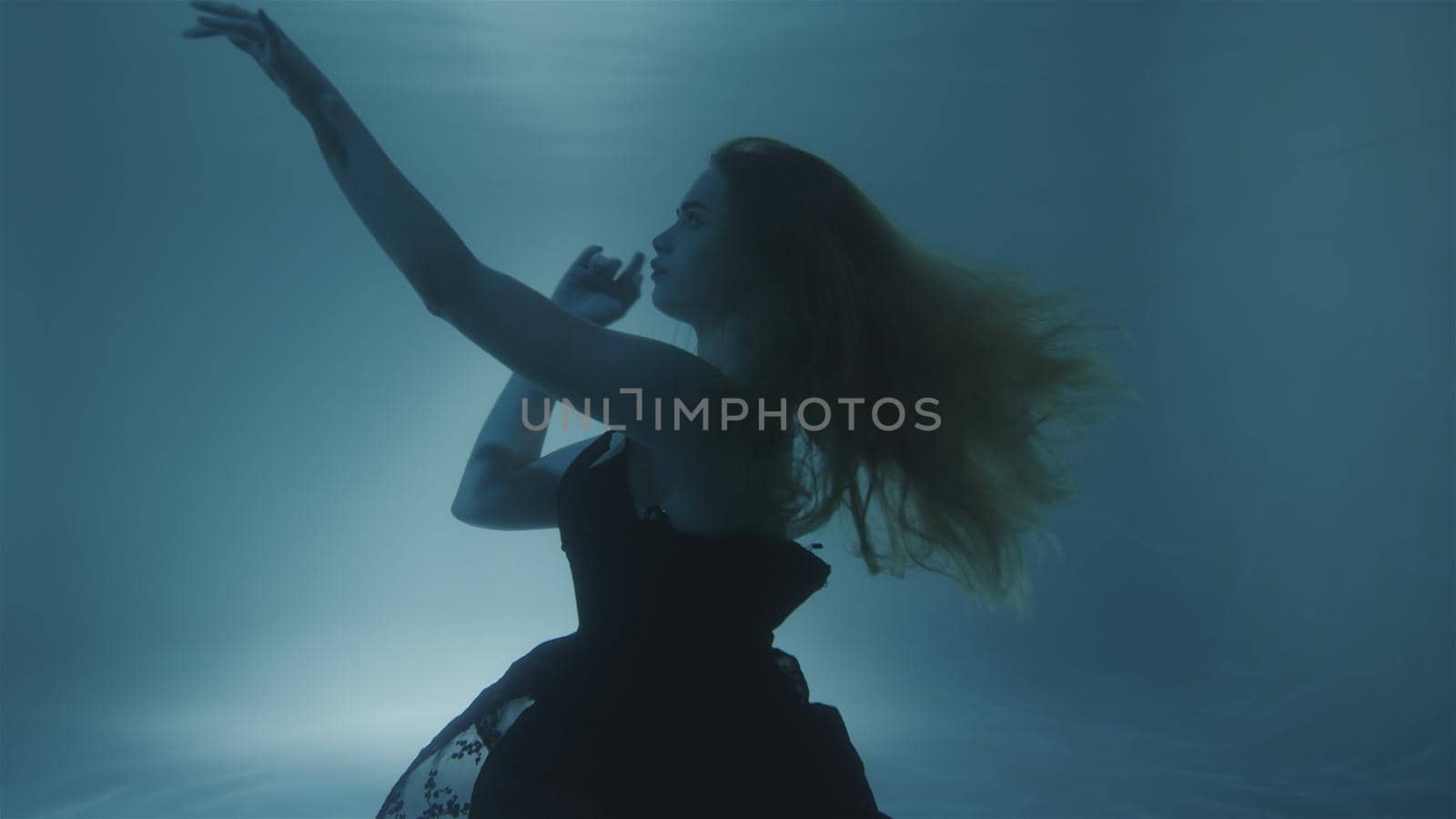 Woman with red hair posing in black dress underwater by studiodav