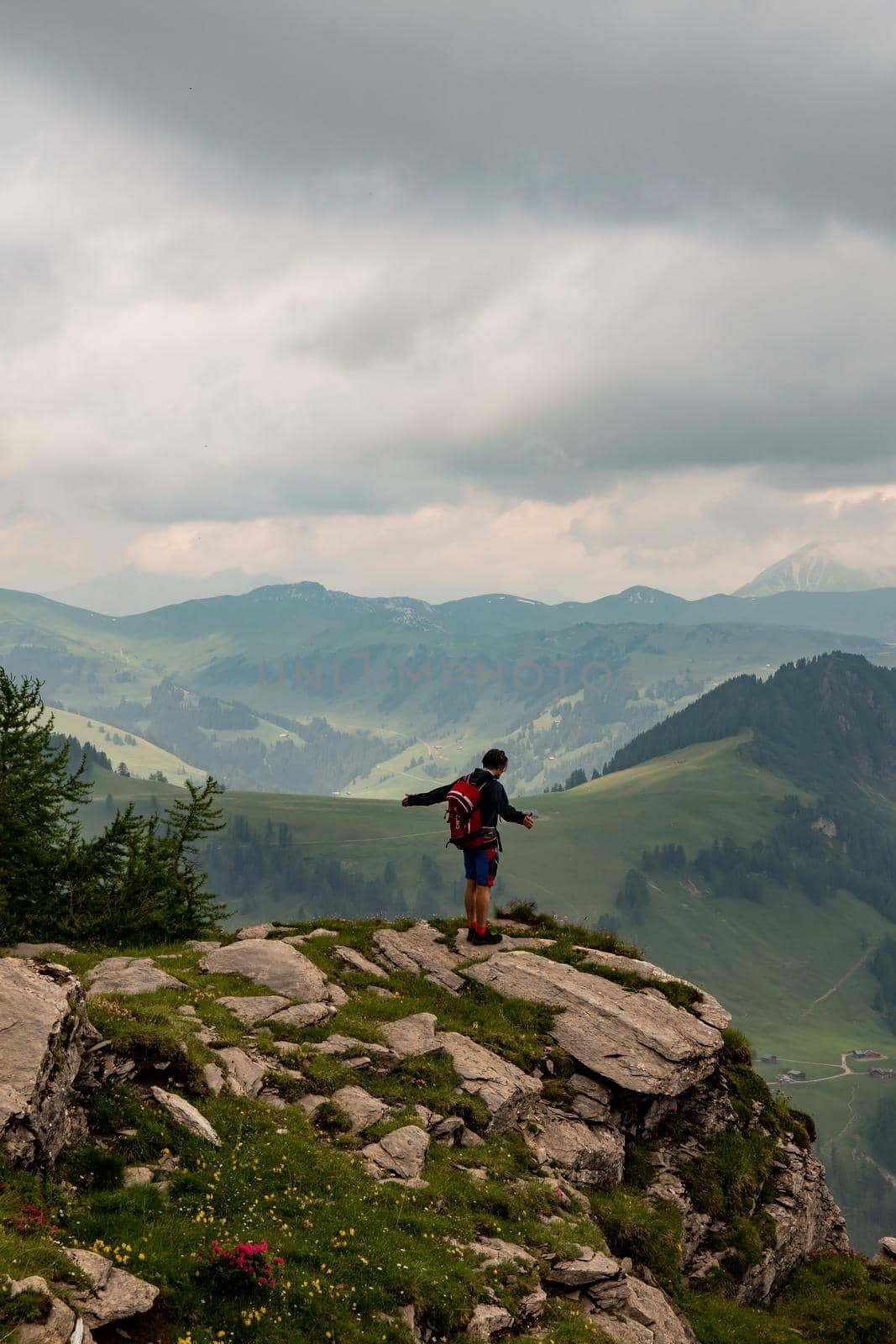 a guy standing at the cliff of a mountain, holding out both of his arms looking into the distance. High quality photo. Panorama over the bernese oberland in the swiss alps.