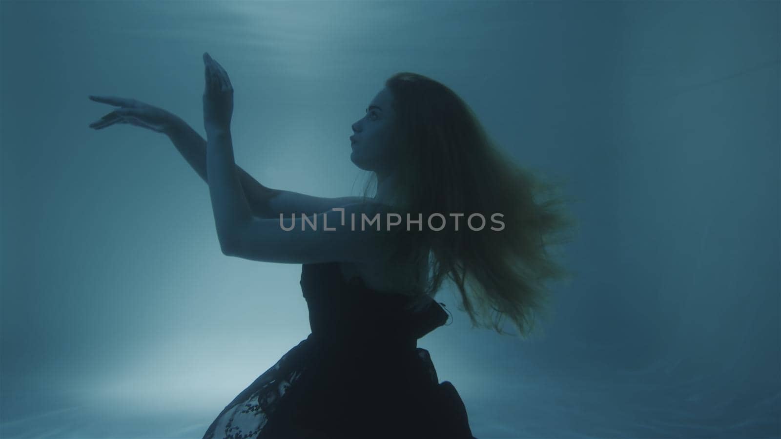 Woman with red hair posing in black dress underwater in 4k