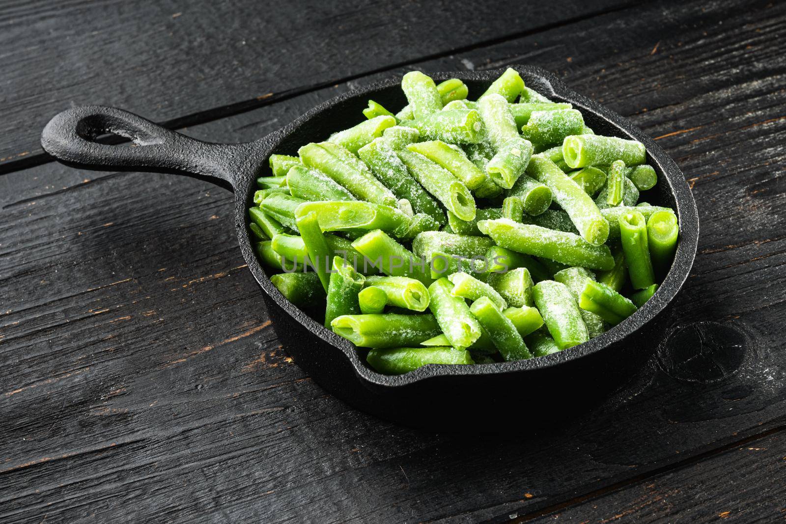 Frozen organic green beans. Healthy food concept set, in frying cast iron pan, on black wooden table background