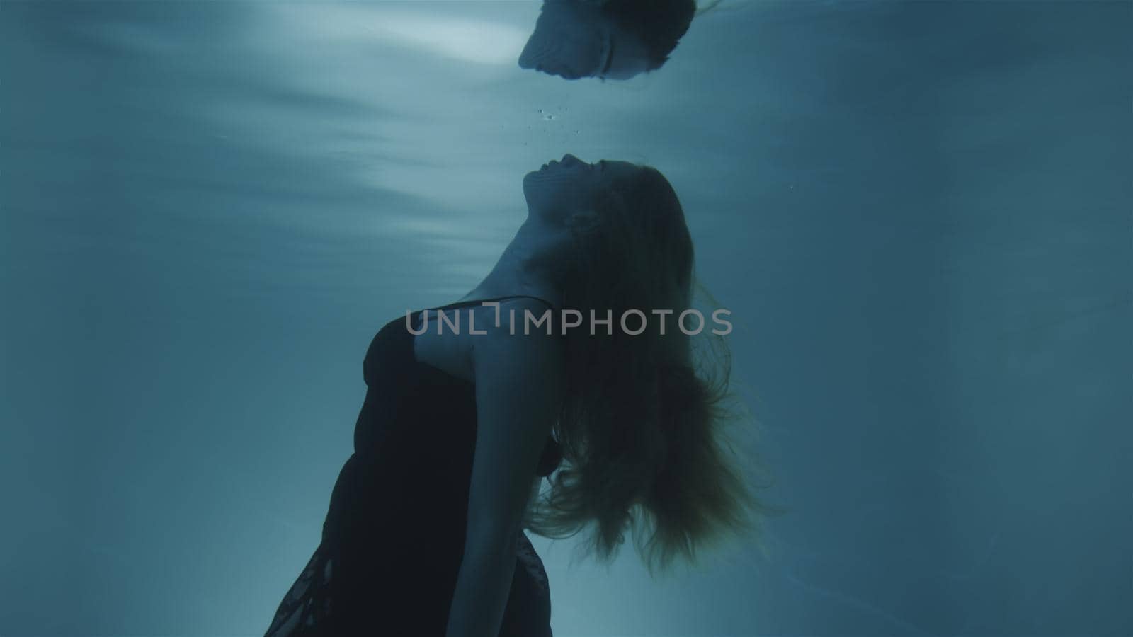 Woman with red hair posing in black dress underwater by studiodav