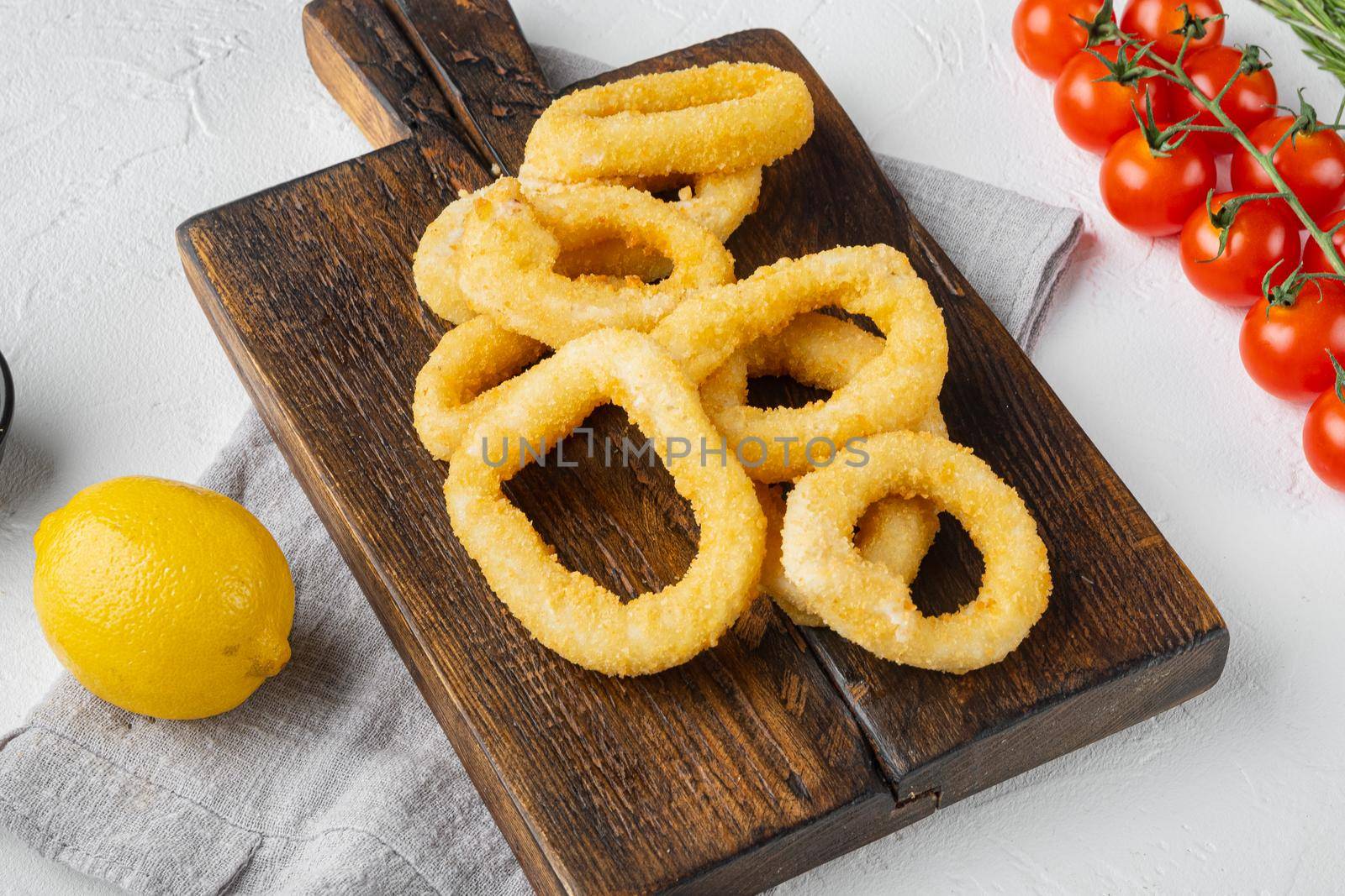 Fried squid rings breaded, on serving board, on white stone table background by Ilianesolenyi