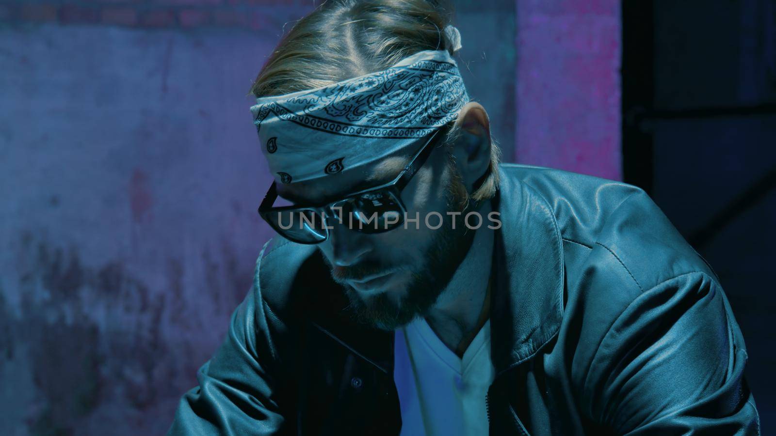 Male biker in a bandana in sunglasses against a brick wall with a neon sign 4k