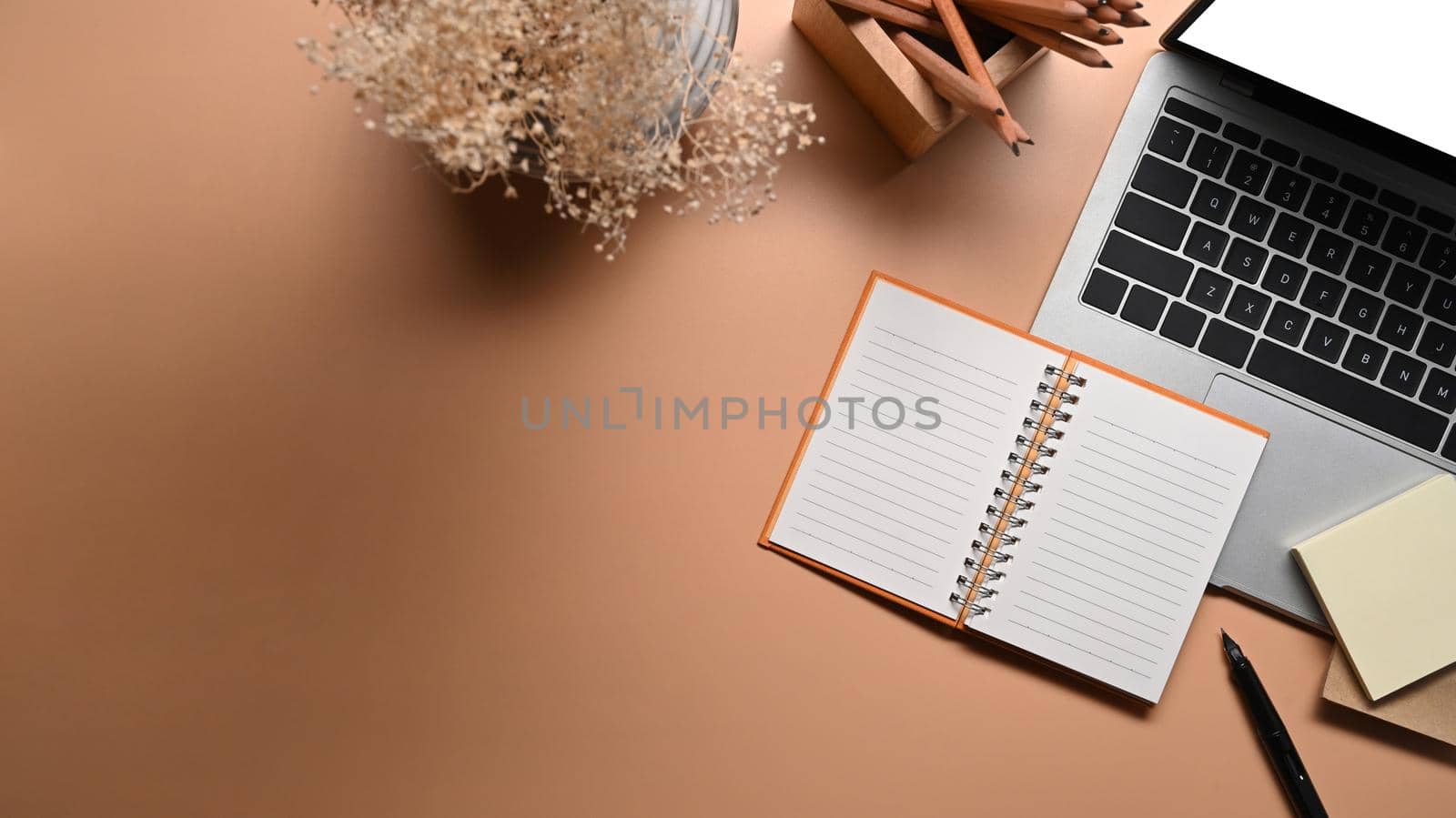 Stylish workspace with laptop, notebook, stick notes and pencil holder on beige background. by prathanchorruangsak