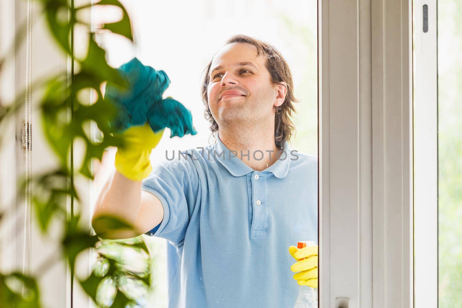 Man wearing yellow protective gloves cleaning windows at home. Doing home chores routine. Selective focus on the face