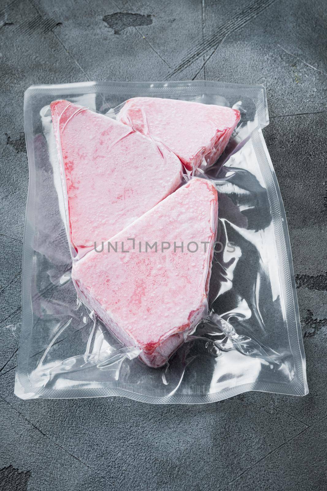 Frozen Tuna fish steak in a vacuum plastic package, on gray stone background by Ilianesolenyi
