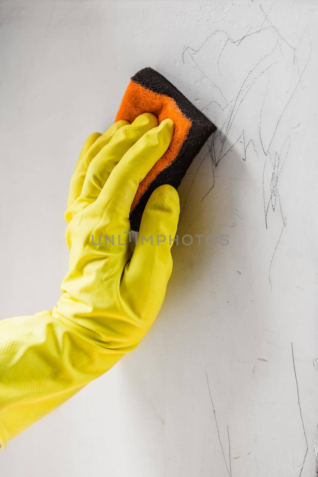 Female hand wearing the protective ruber gloves cleaning the child pencil drawings from the wall