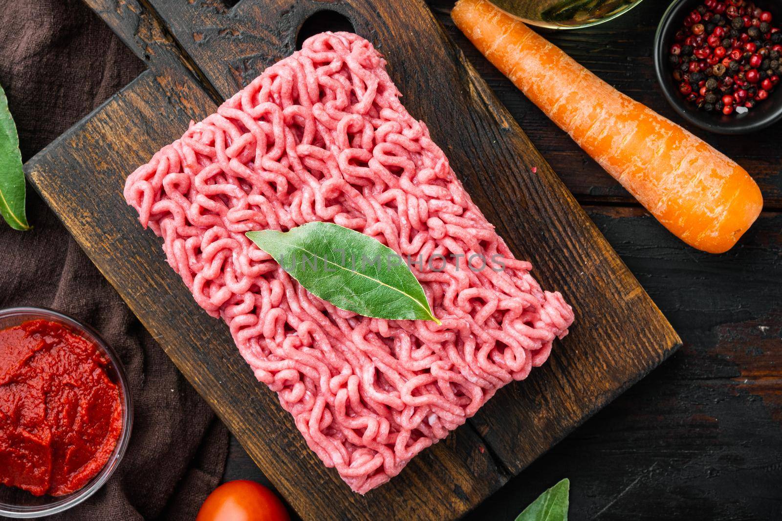 Traditional italian tomato sauce bolognese with ingredients, minced meat tomatoe and herbs, on wooden cutting board, on old dark wooden table background, top view, flat lay by Ilianesolenyi