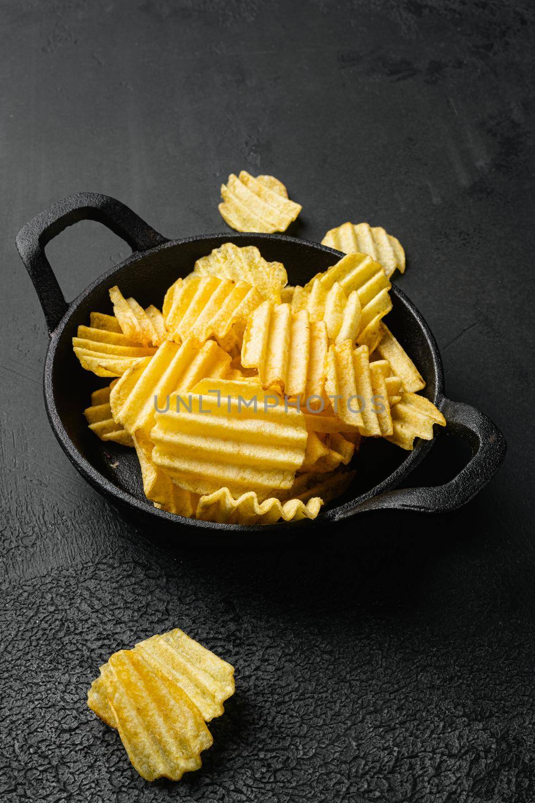 Wavy Lightly Salted Potato Chips, on black dark stone table background