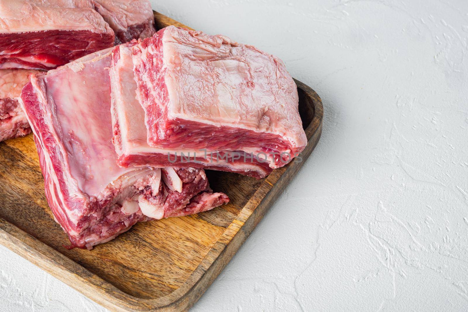 Raw Black Angus Marbled Beef Ribs set, on white stone background, with copy space for text