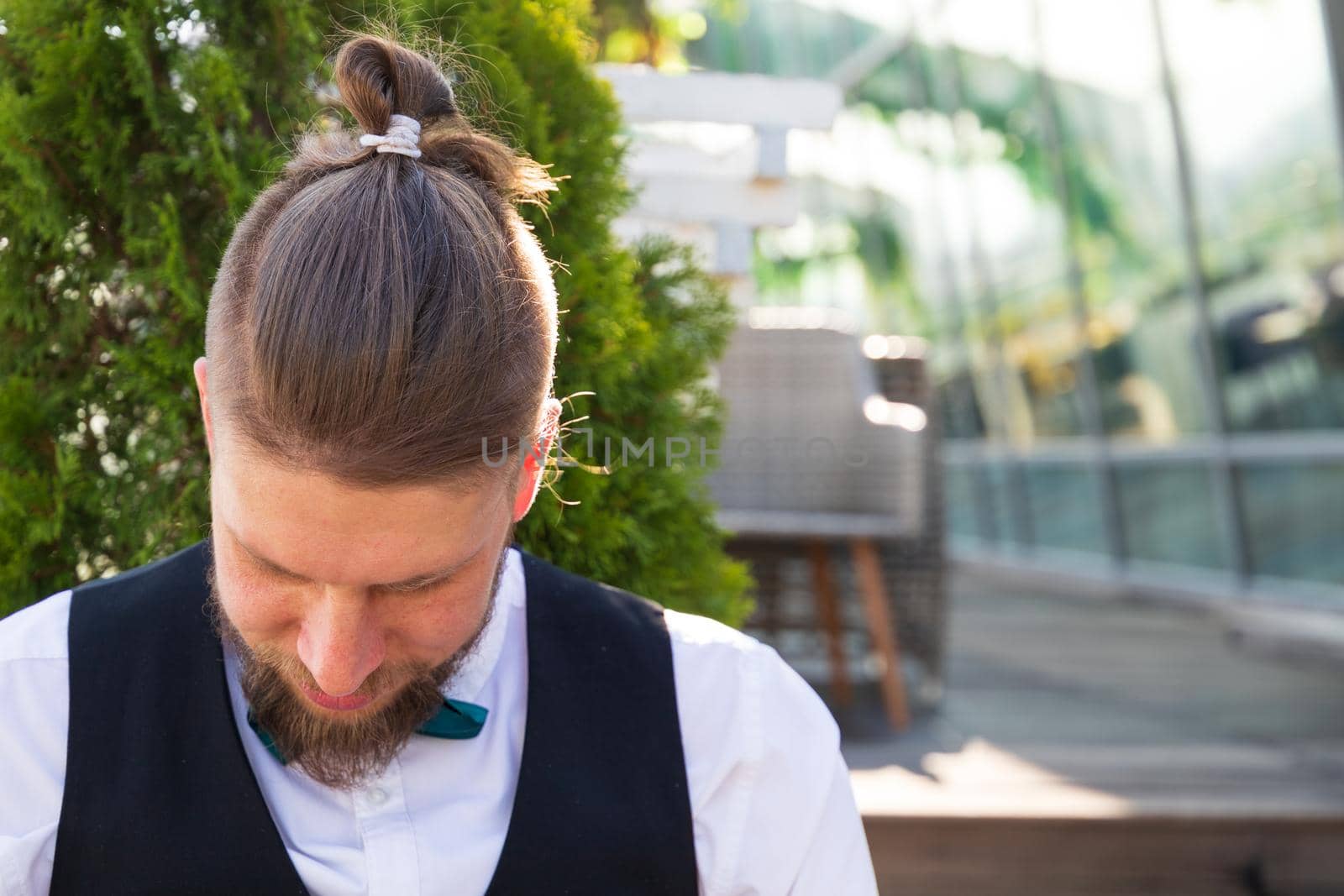 Hipster hairstyle on a young bearded man in a suit sitting in a street cafe.