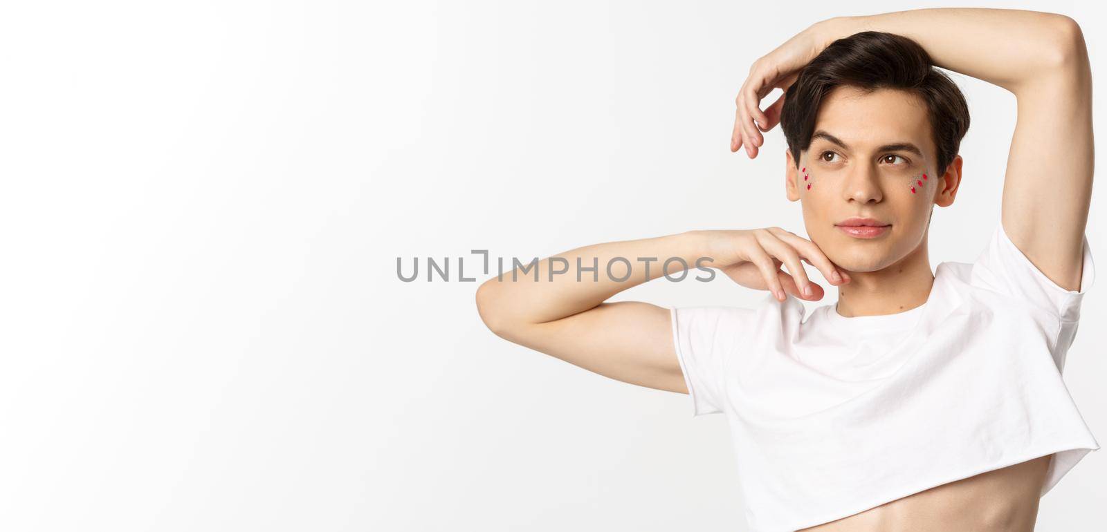 Close-up of beautiful androgynous man in crop top posing for camera, standing against white background by Benzoix