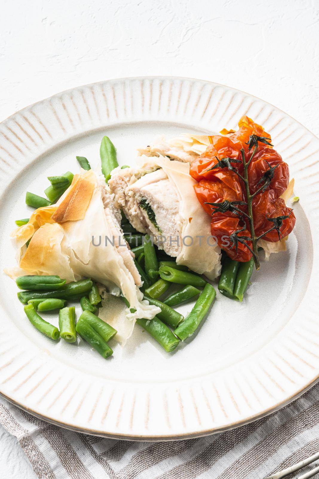 Freshly cooked Chicken Kiev oozing garlic and parsley butter, with baked cherry tomatoes And green beans, on white stone background by Ilianesolenyi