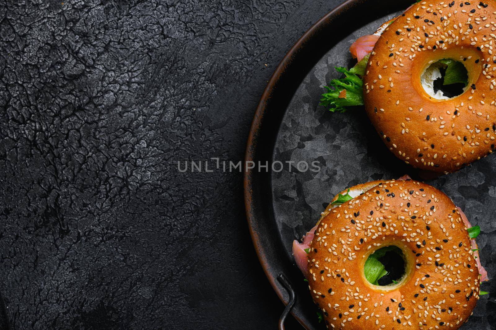 Bagel with red fish and soft cheese, on black dark stone table background, top view flat lay, with copy space for text by Ilianesolenyi
