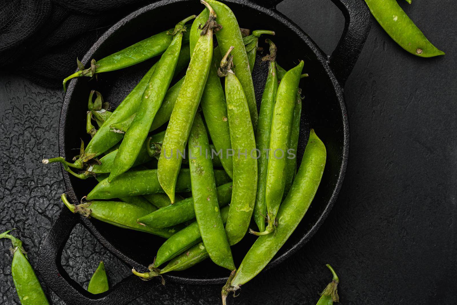 Green pea pod, on black dark stone table background, top view flat lay