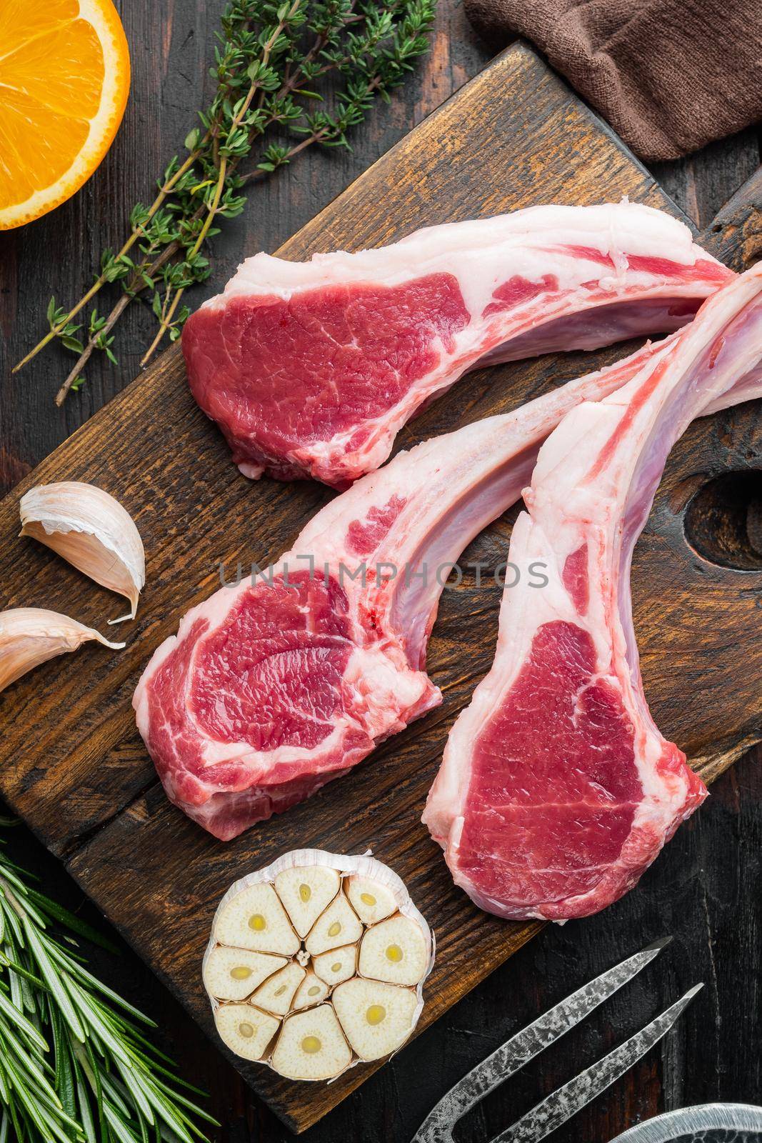 Raw Lamb Filets on bone set, with ingredients carrot orange, herbs, on old dark wooden table background, top view flat lay