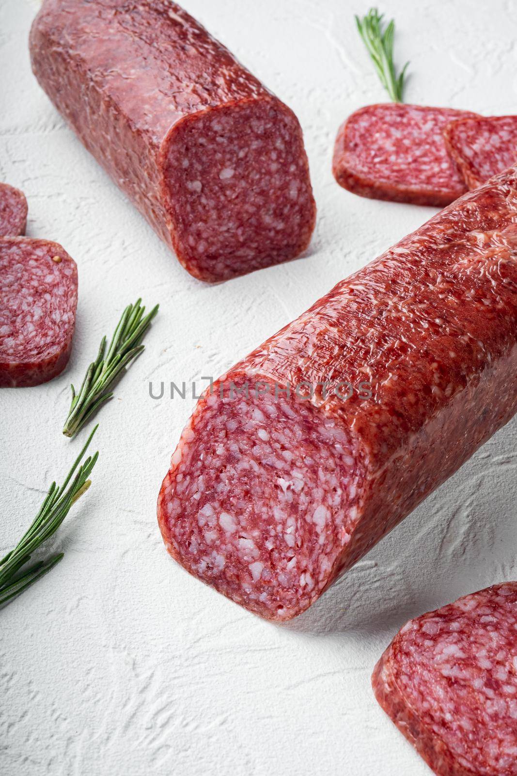 Slices of salami with vegetables, on white stone table background by Ilianesolenyi