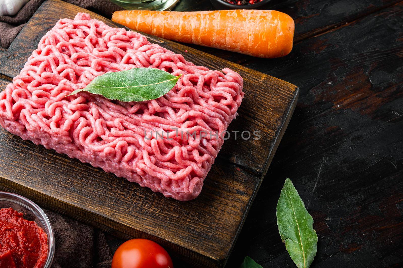 Classic italian bolognese sauce ingredients, ground meat tomatoe and herbs, on wooden cutting board, on old dark wooden table background, with copy space for text by Ilianesolenyi