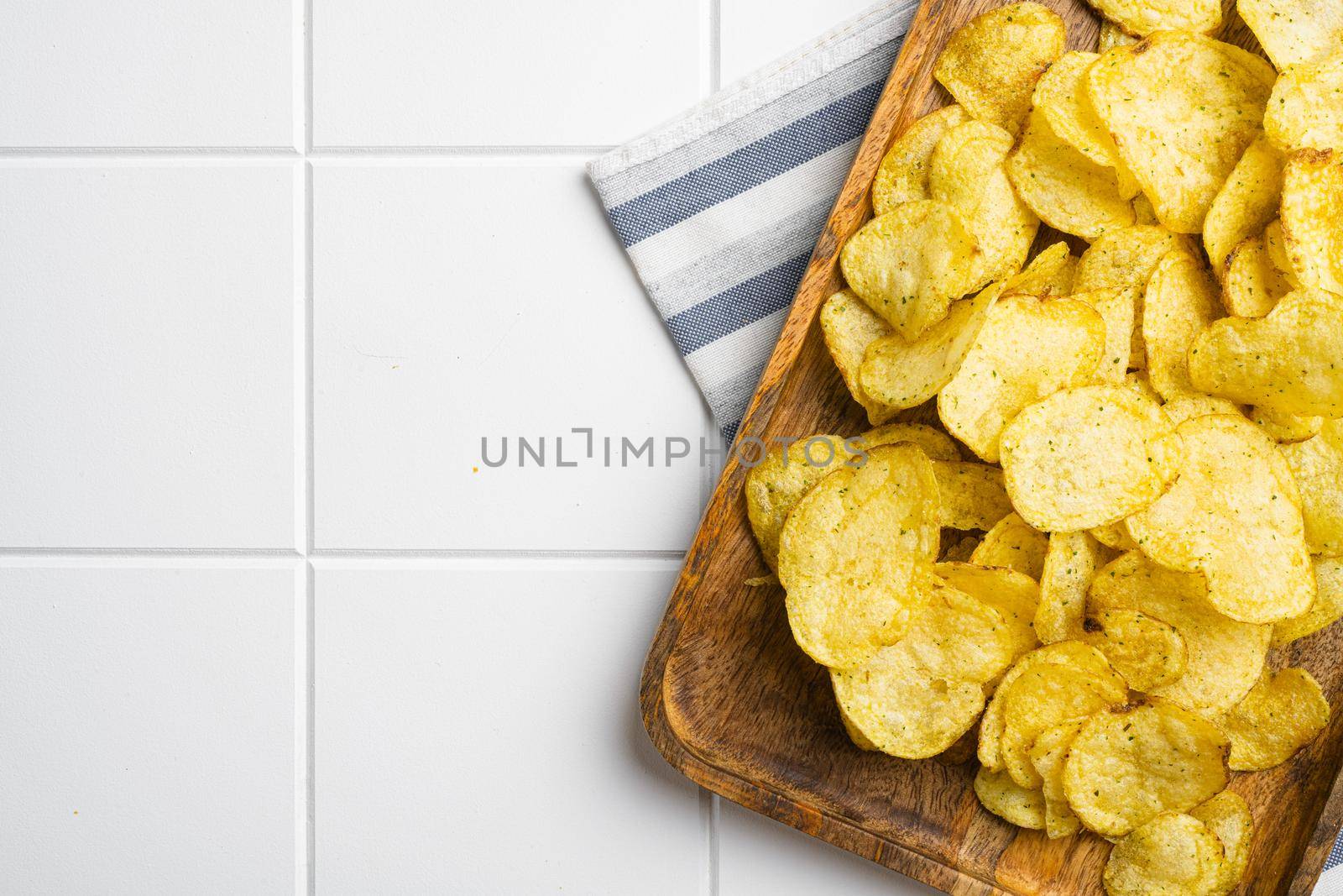 Home made potato chips on white ceramic squared tile table background, top view flat lay, with copy space for text by Ilianesolenyi