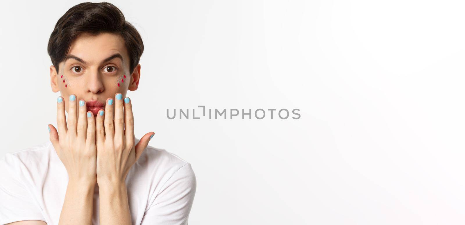 People, lgbtq and beauty concept. Beautiful gay man showing blue nail polish on fingernails and looking at camera, have manicure, standing over white background by Benzoix