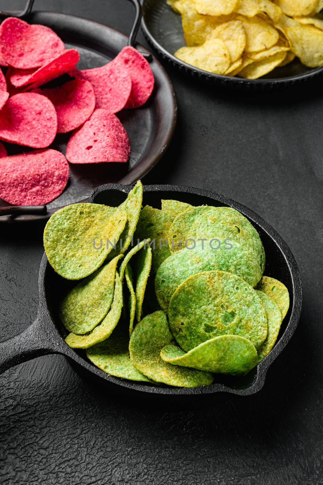 Green potato chips, on black dark stone table background