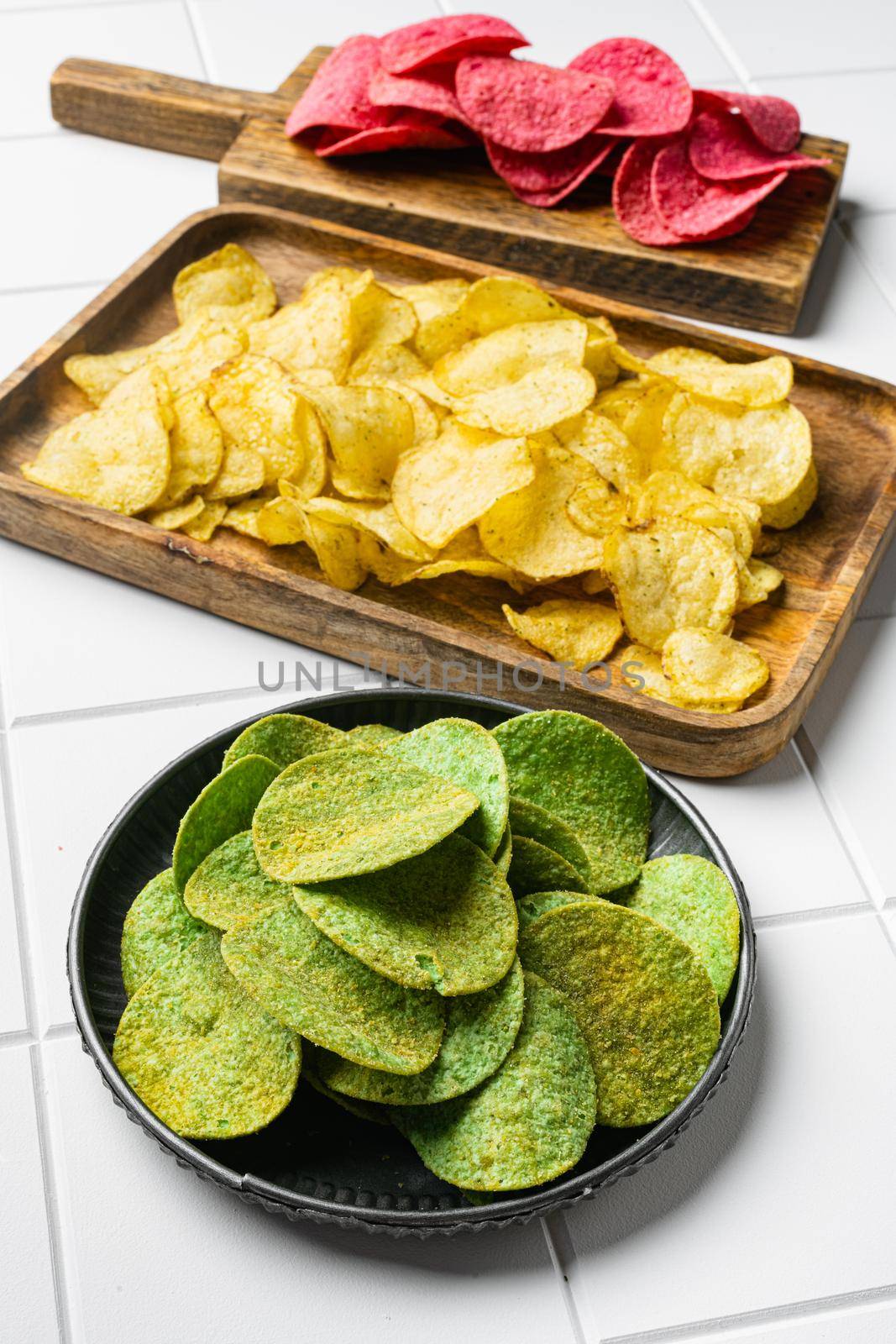 Green potato chips, on white ceramic squared tile table background