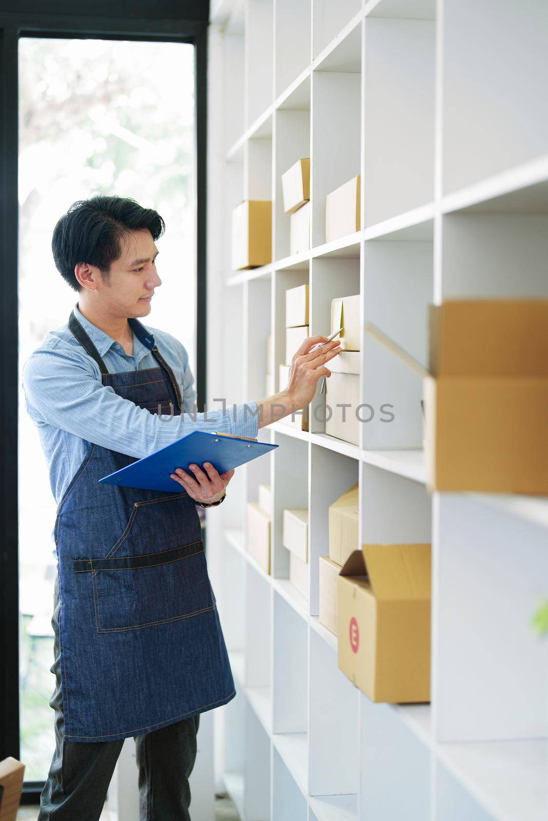 A portrait of a small startup, an SME owner, an Asian male entrepreneur checking orders to arrange the produce before packing the products in the inner boxes with the customers. Freelance concepts.