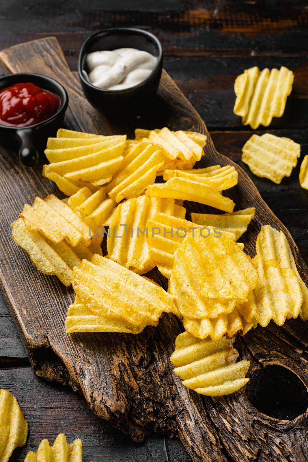 Wavy Salt Pepper Flavored Potato Chips on old dark wooden table background by Ilianesolenyi