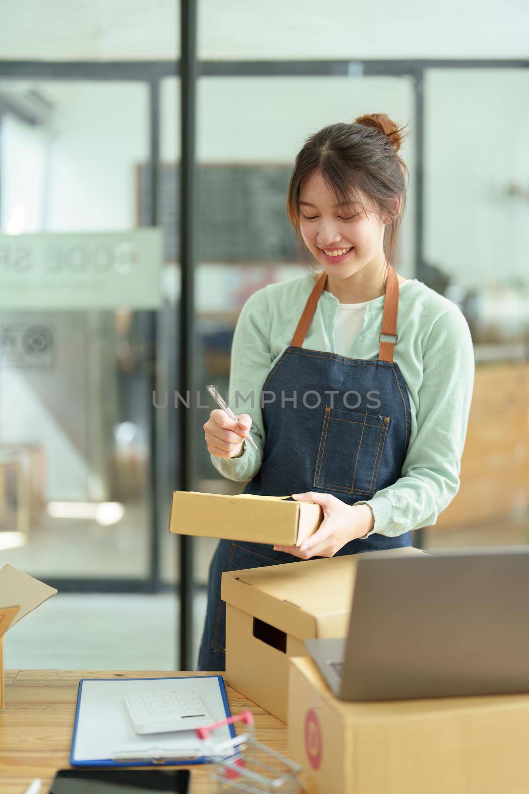 A portrait of a small startup, and SME owner, an Asian female entrepreneur, is writing down information on a notepad to organize the product before packing it into the inner box for the customer.