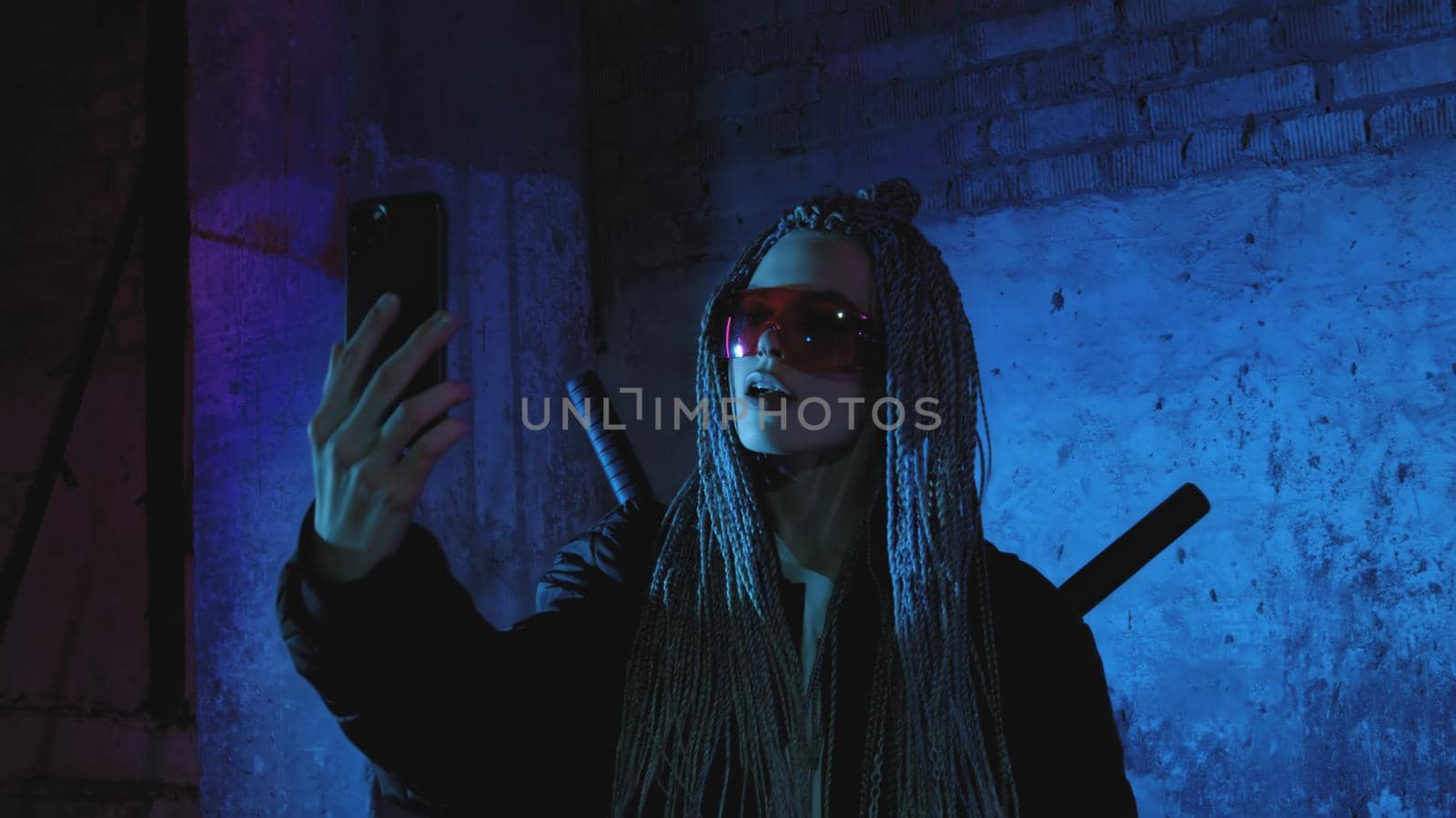 a girl with dreadlocks and katanas stands by a neon brick wall and takes a selfie on a mobile phone by studiodav