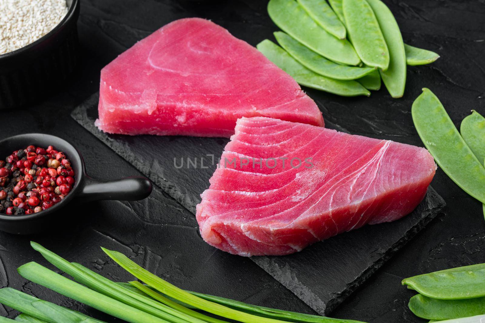 Pieces of raw tuna with ingredients green pea, sesame and herbs set, on stone board, on black stone background