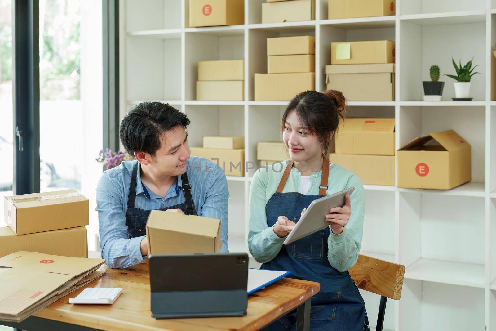 Portrait of a small start-up and SME owner, an Asian male and female entrepreneur checking orders and packing for customers, self-employed, freelance, online selling.