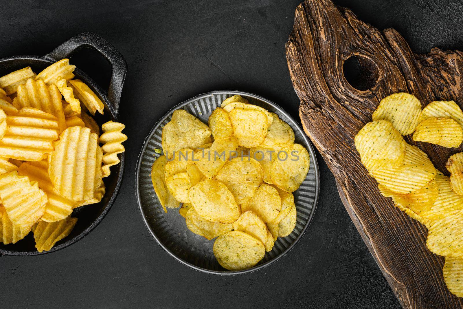 Cheddar Sour Cream Flavored Potato Chips, on black dark stone table background, top view flat lay