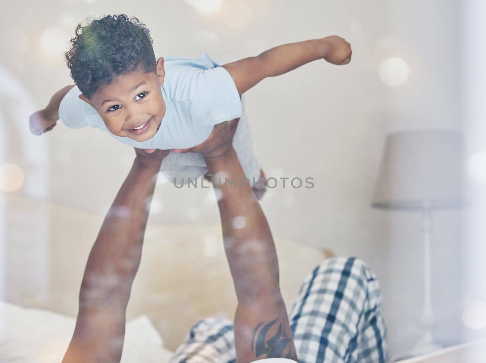 Happy little mixed race boy flying in fathers arms looking at camera in bedroom. Dad holding and lifting cute little child playing and having fun on bed.