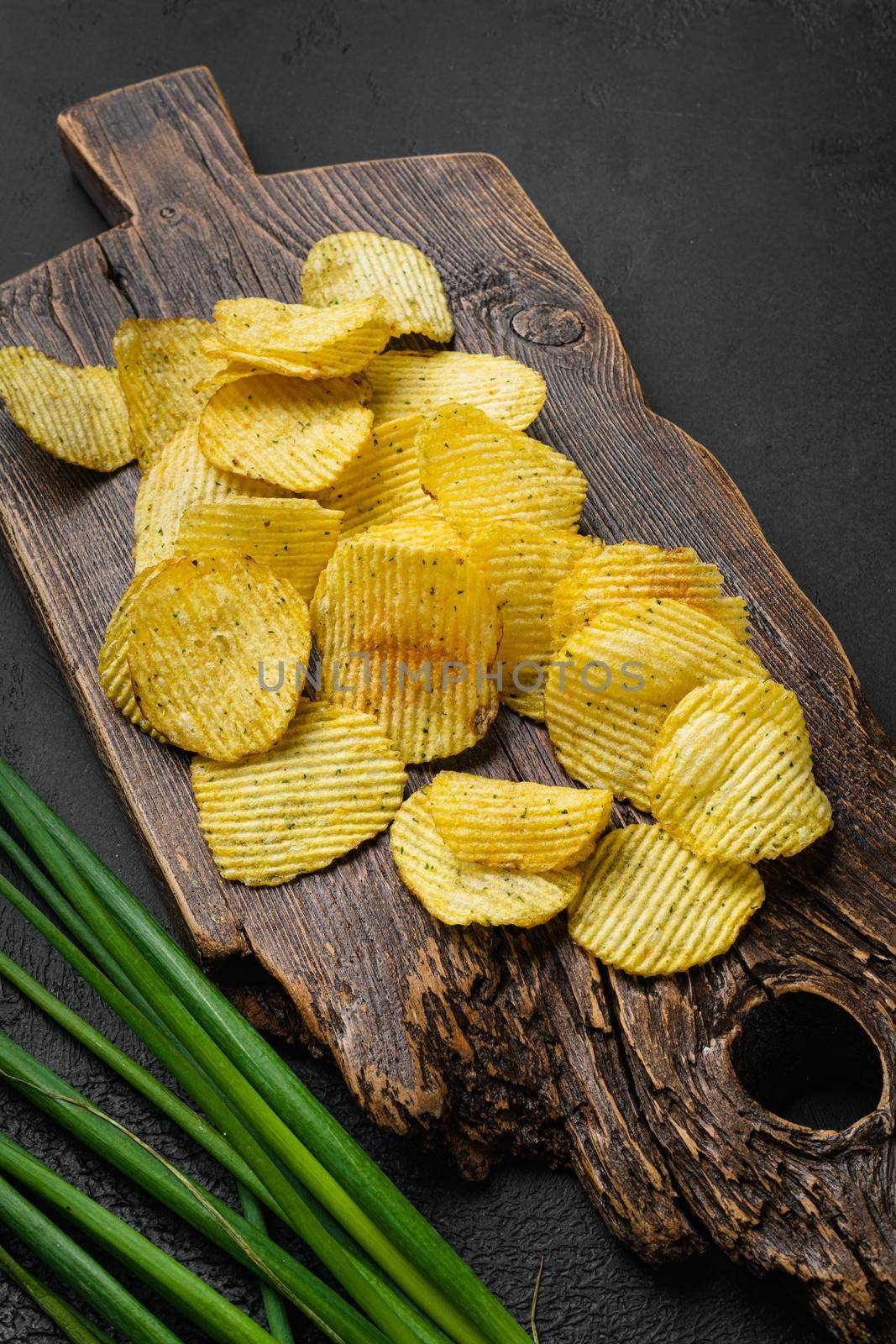 Wavy Potato Chips on black dark stone table background by Ilianesolenyi