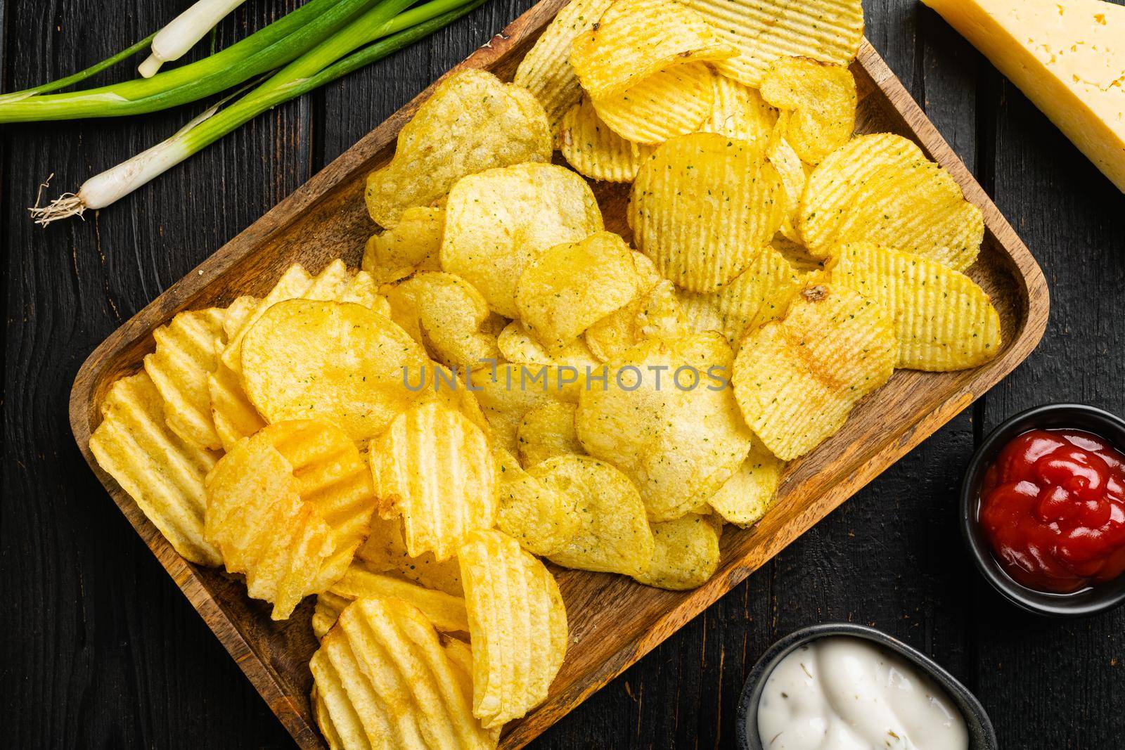 Variation different potato chips, on black wooden table background, top view flat lay