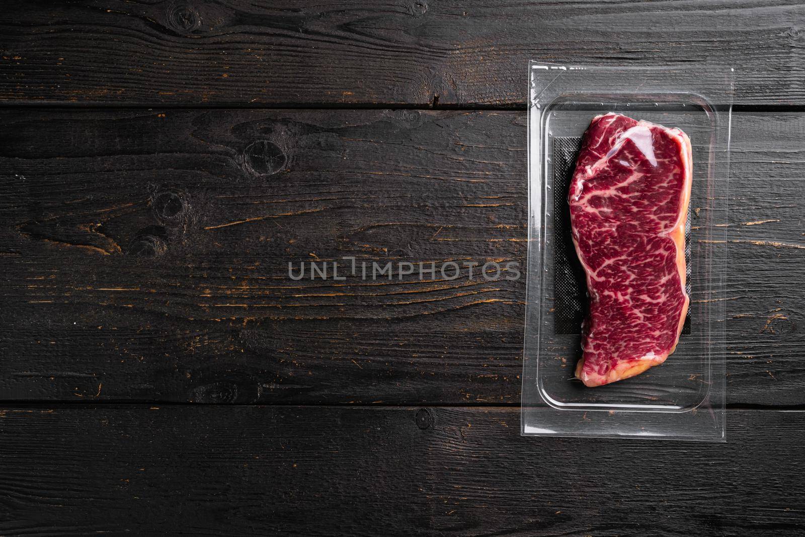 Raw Striploin marbled beef steak vacuum Packed set, on black wooden table background, top view flat lay, with copy space for text