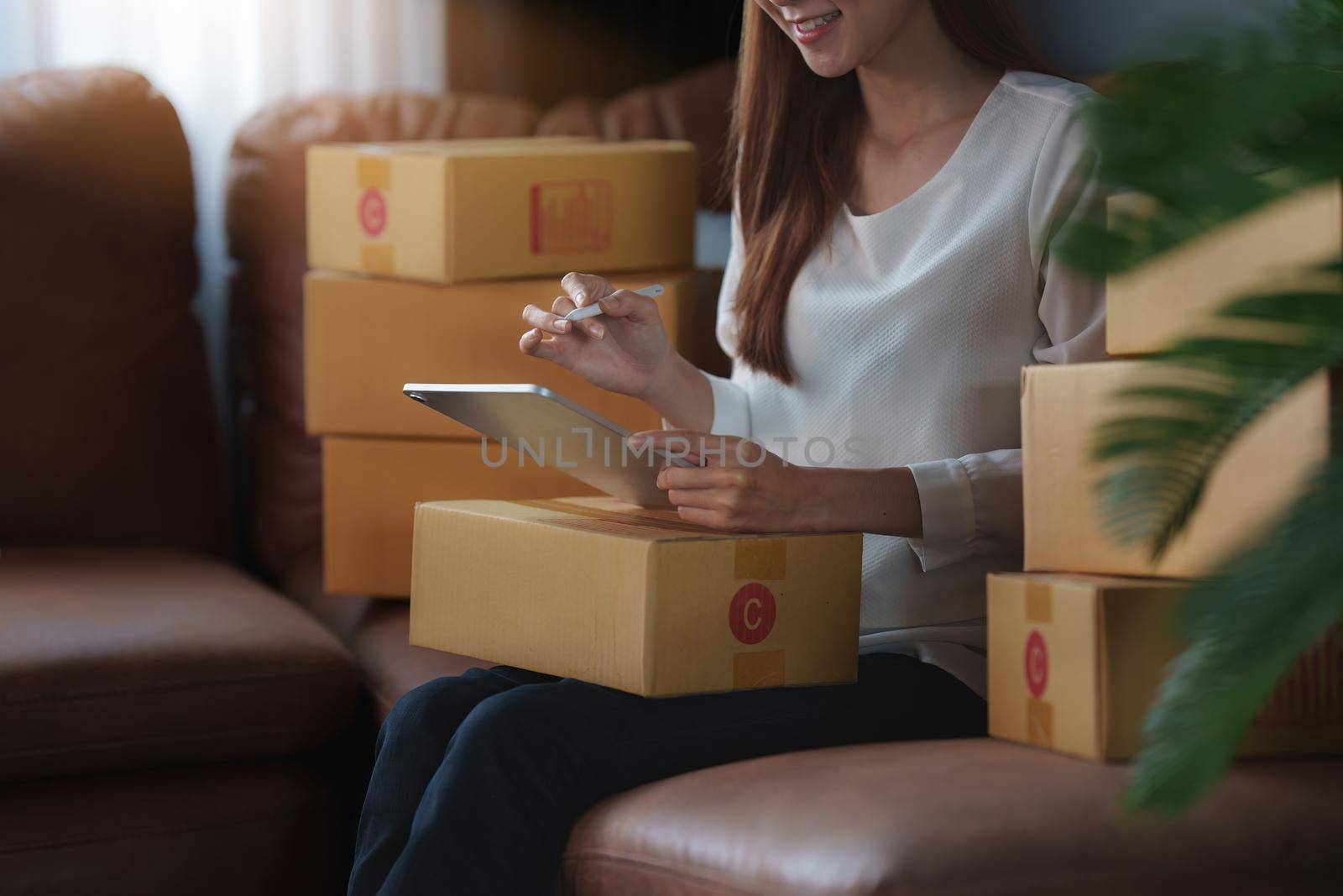 Image of Young asian woman startup freelance with parcel box and talking with customer by tablet. Online marketing packing box delivery concept
