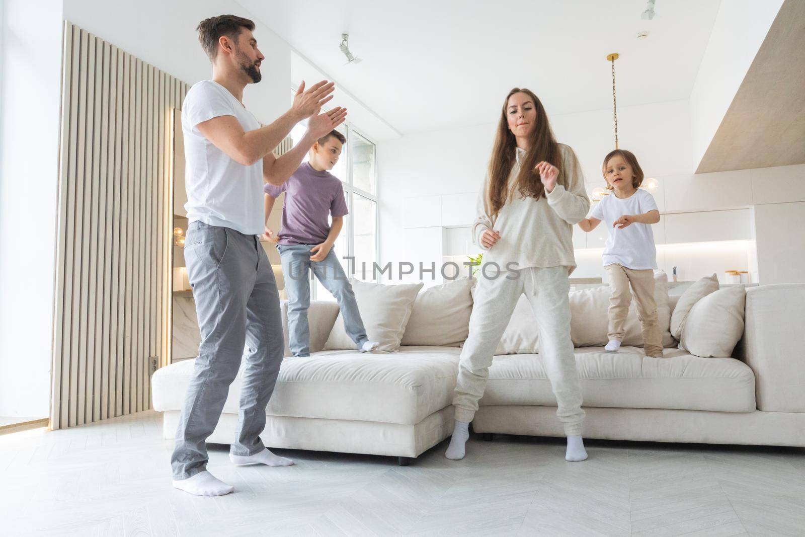 Funny active family of four young adult parents and cute small children dancing together in living room interior, carefree little kids with mum dad having fun laughing enjoy leisure at home