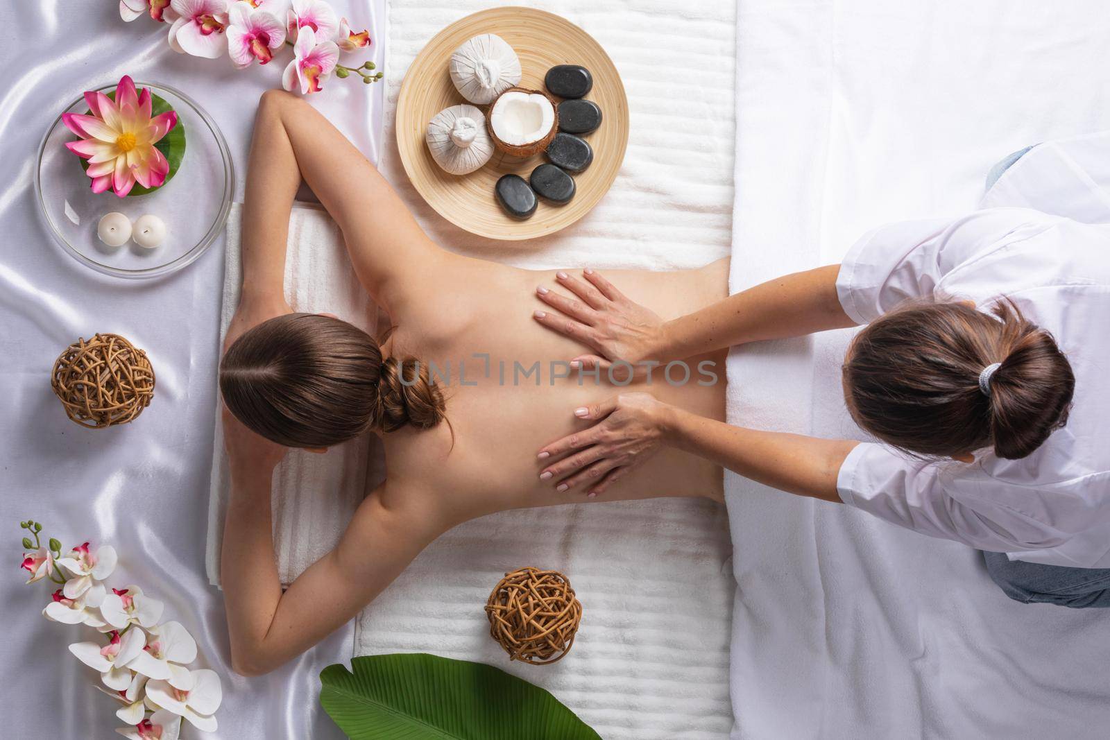 Woman at spa thai massage tow view, beauty treatments concept. Orchid and lotus flowers coconut stones and herb pouches
