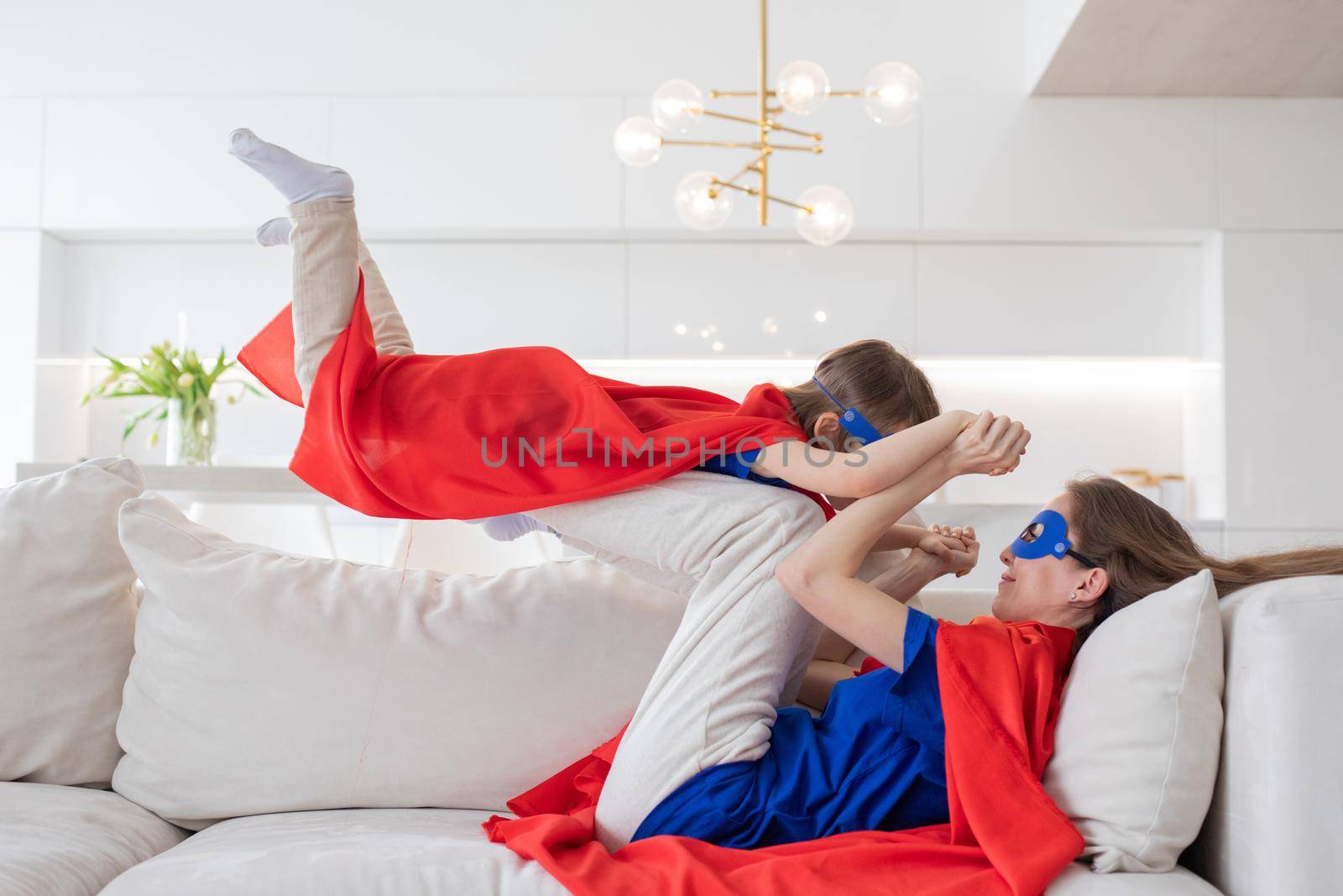 Mother holding daughter flying in superhero costume at home