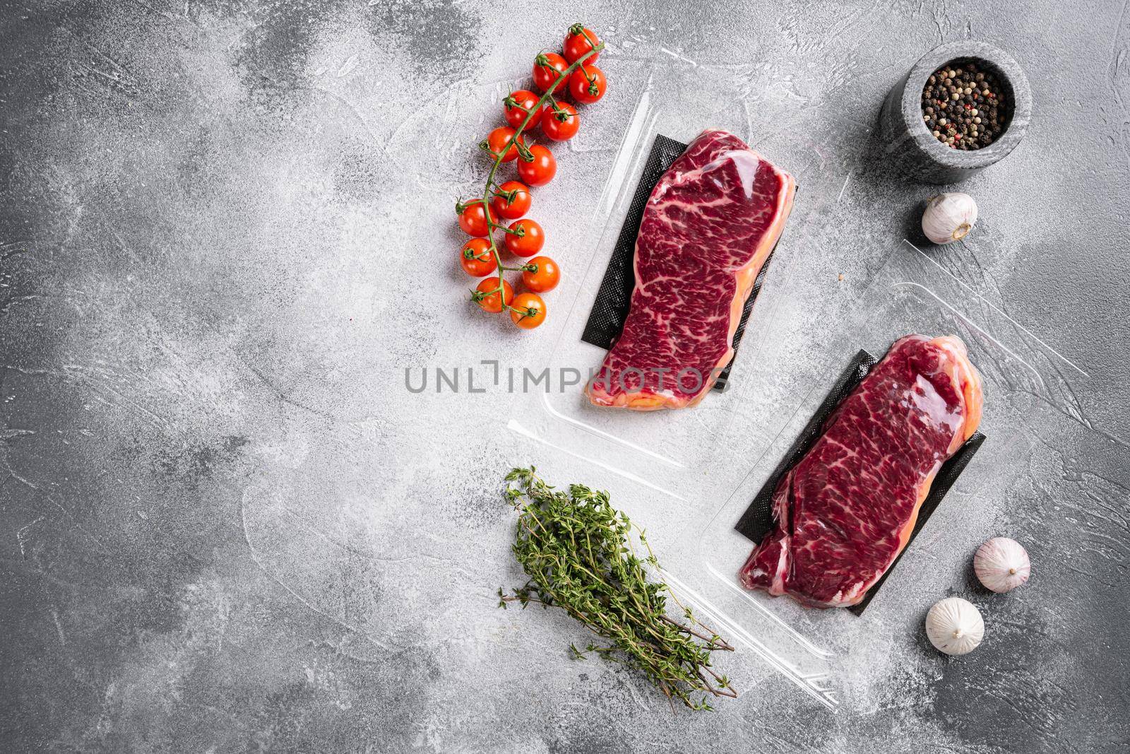 Raw marbled beef steaks in vacuum pack, on gray stone table background, top view flat lay, with copy space for text by Ilianesolenyi