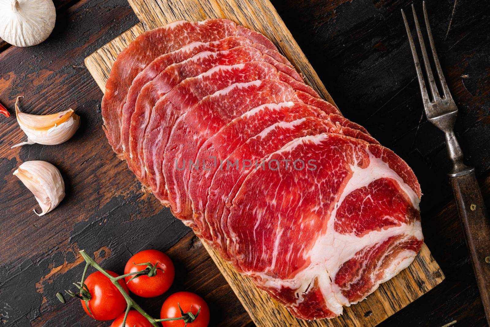 Cured meat, pork neck, coppa set, on old dark wooden table background, top view flat lay