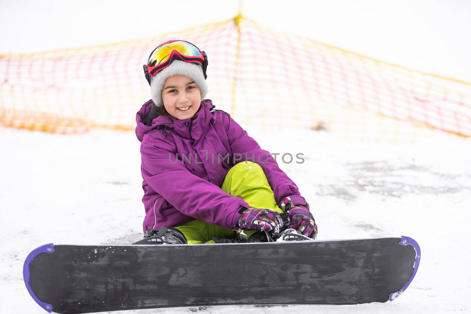 Snowboard Winter Sport. Little kid girl playing with snow wearing warm winter clothes. Winter background.