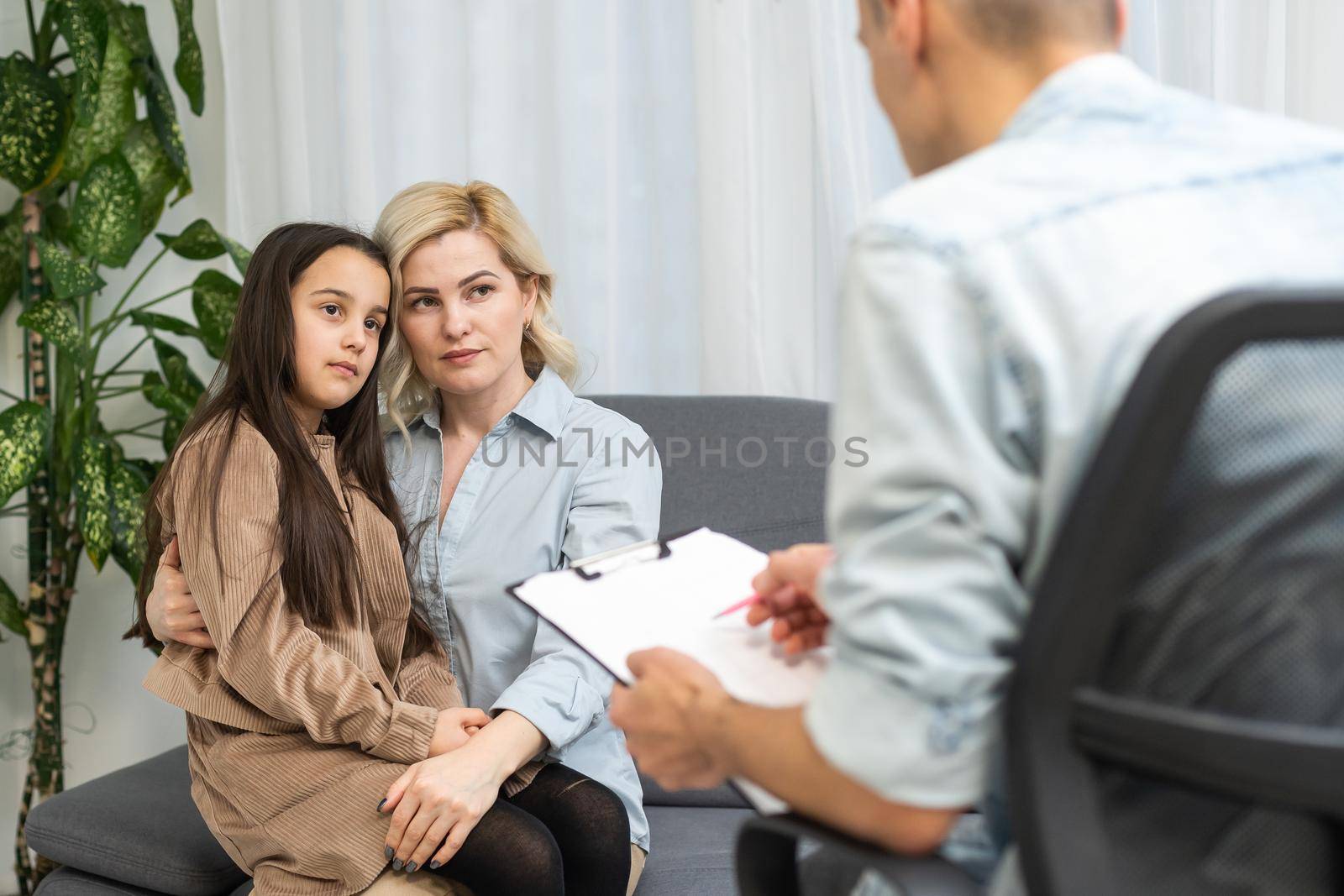 Female psychologist counseling parent. Serious single mom and sad unhappy child sitting on sofa and discussing social behaviour, ADHD disorder diagnosis, apathy or adolescent depression with therapist.