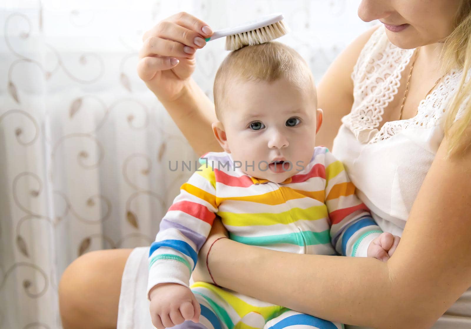 The mother is combing the little baby's hair. Selective focus. People.