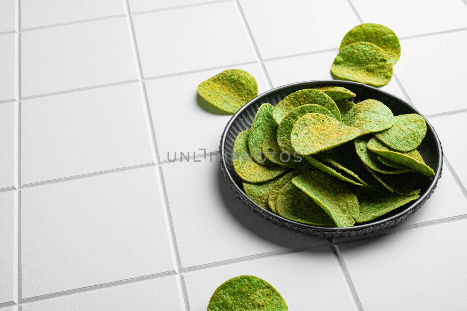 Green Cheddar Jalapeno crispy bite Potato Chips on white ceramic squared tile table background, with copy space for text by Ilianesolenyi