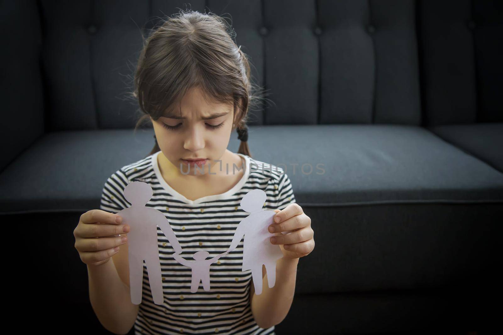 Child with a paper family in his hands. the concept of divorce, custody and child abuse. Selective focus. by yanadjana