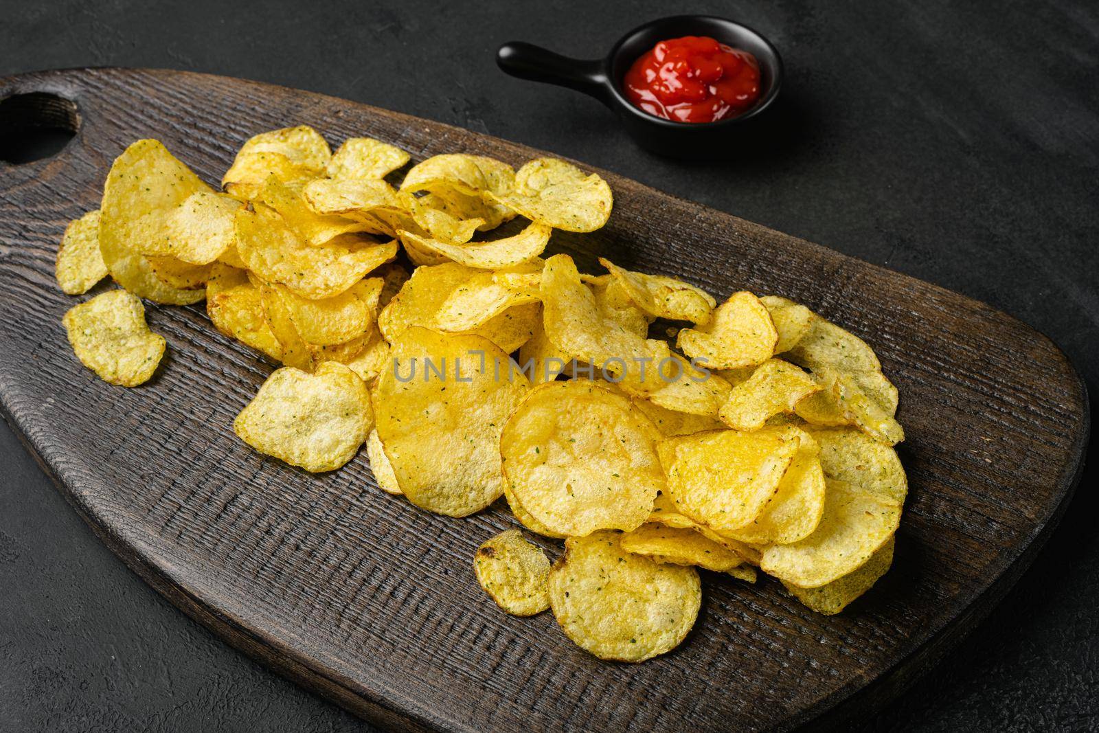 Crispy potato chips on black dark stone table background by Ilianesolenyi