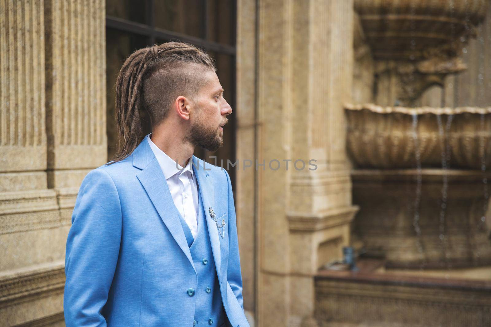 Caucasian man with dreadlocks in blue three piece business suit, outdoor portrait.